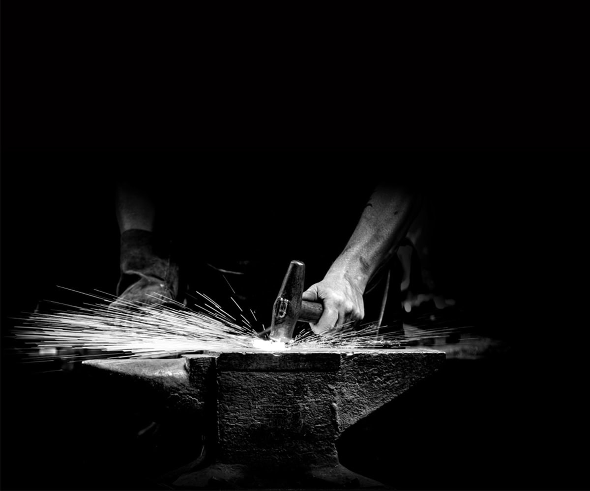 Hand mit Hammer schlägt auf Amboss